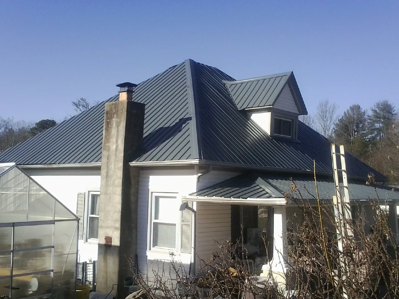 Dark blue standing seam metal roof on a white farmhouse with dormer — Slate & Tile Roof Repair by Roofing Brothers in Cumming
