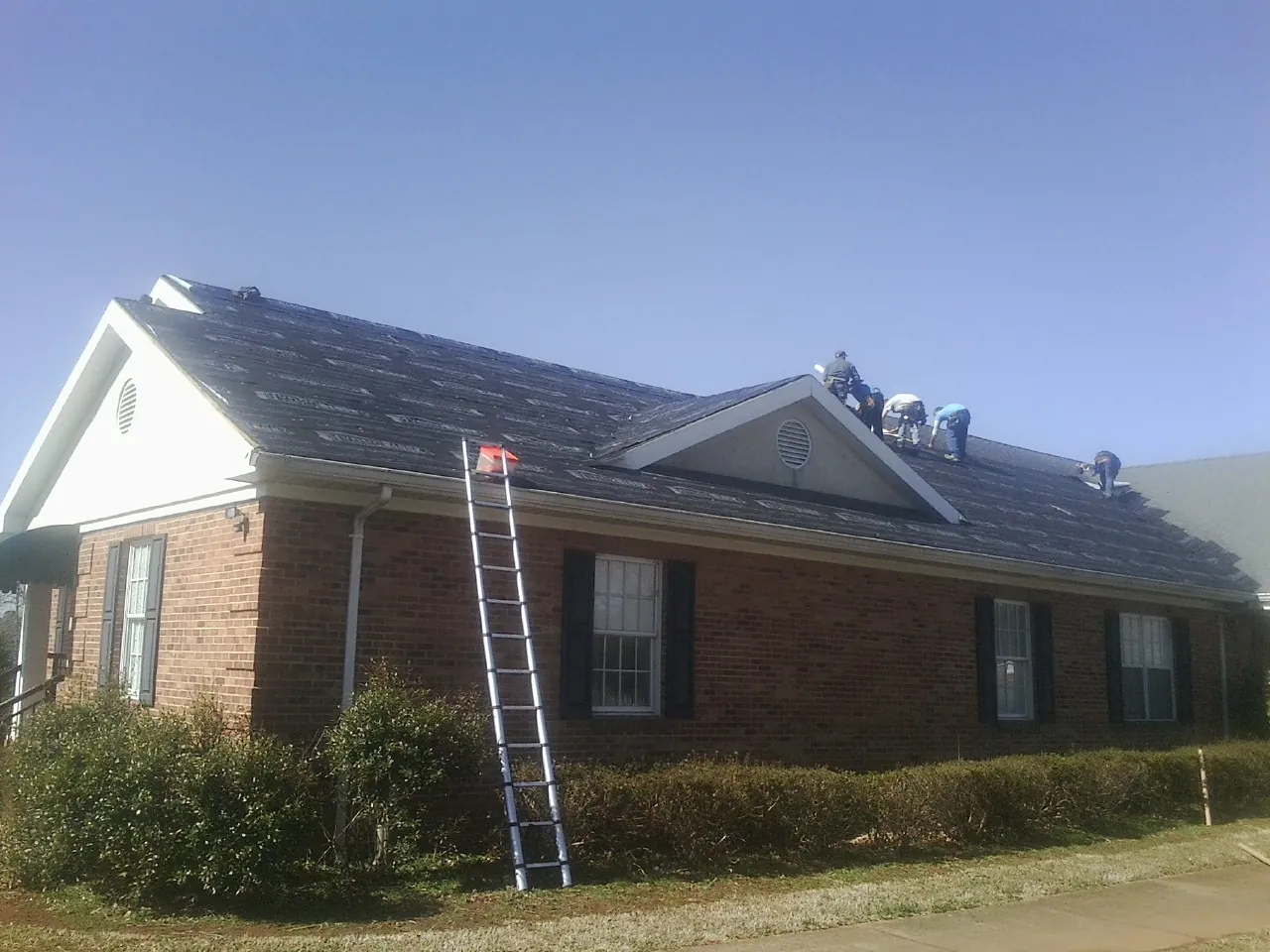 Crew tearing shingles off a brick ranch roof with a ladder set — Emergency Roof Repair work by our crew in Cumming