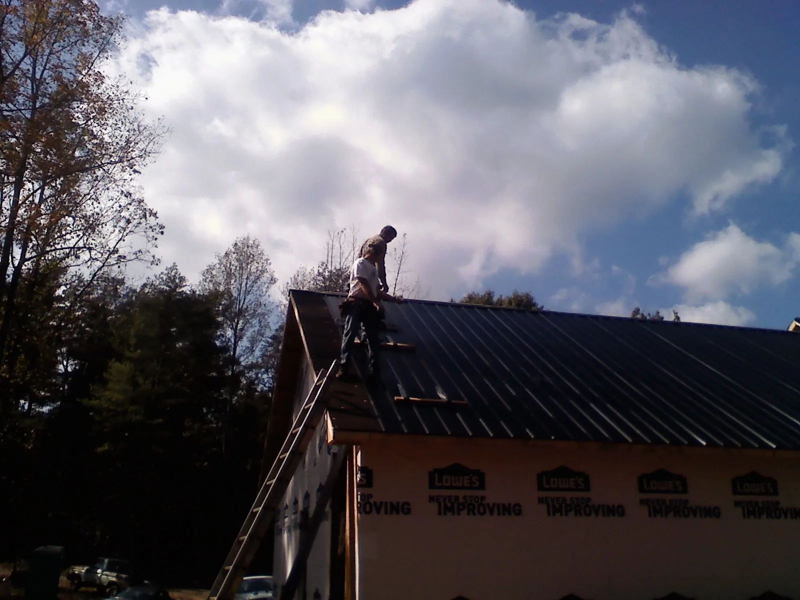 Roofer fastening dark metal panels high against a cloudy sky, from a Roof Inspection job in Cumming