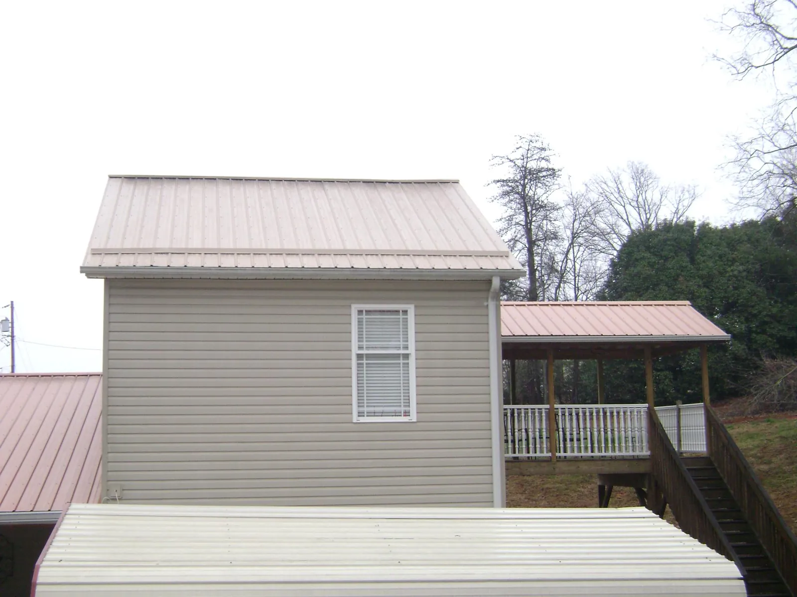 Tan metal roofs on a two story addition and attached porch, from a Roof Replacement job in Cumming